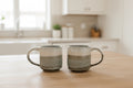 Two ceramic mugs on a wooden table with a home interior background