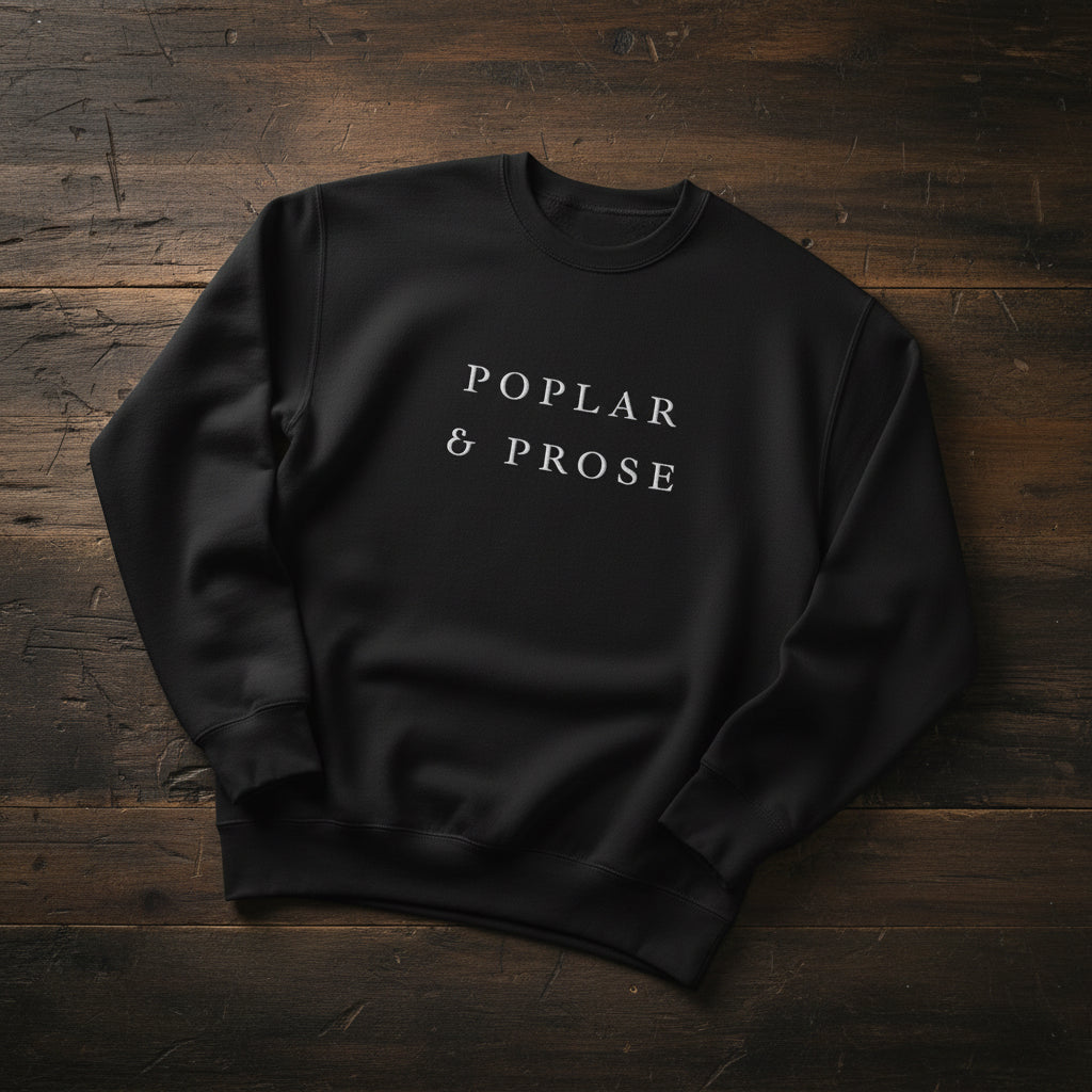 Black sweatshirt with 'Poplar & Prose' text on a wooden surface