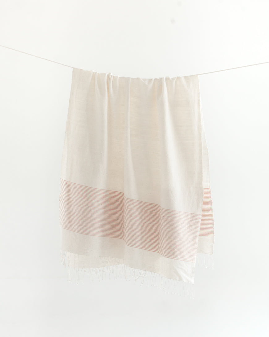 White-cream towel with blush stripe draped over a white surface
