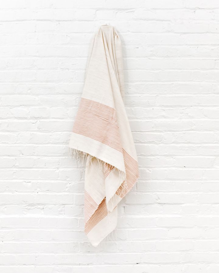 Towel with blush and white stripes hanging on a white wooden wall