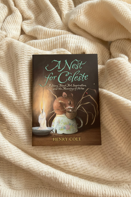 A book titled "A Nest for Célesté" by Henry Cole, featuring an illustration of a small brown mouse in a floral teacup with a candle and spider details, placed on a textured cream knit blanket.