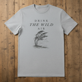 Gray t-shirt with 'Drink the Wild Air' text and tree graphic on a wooden surface