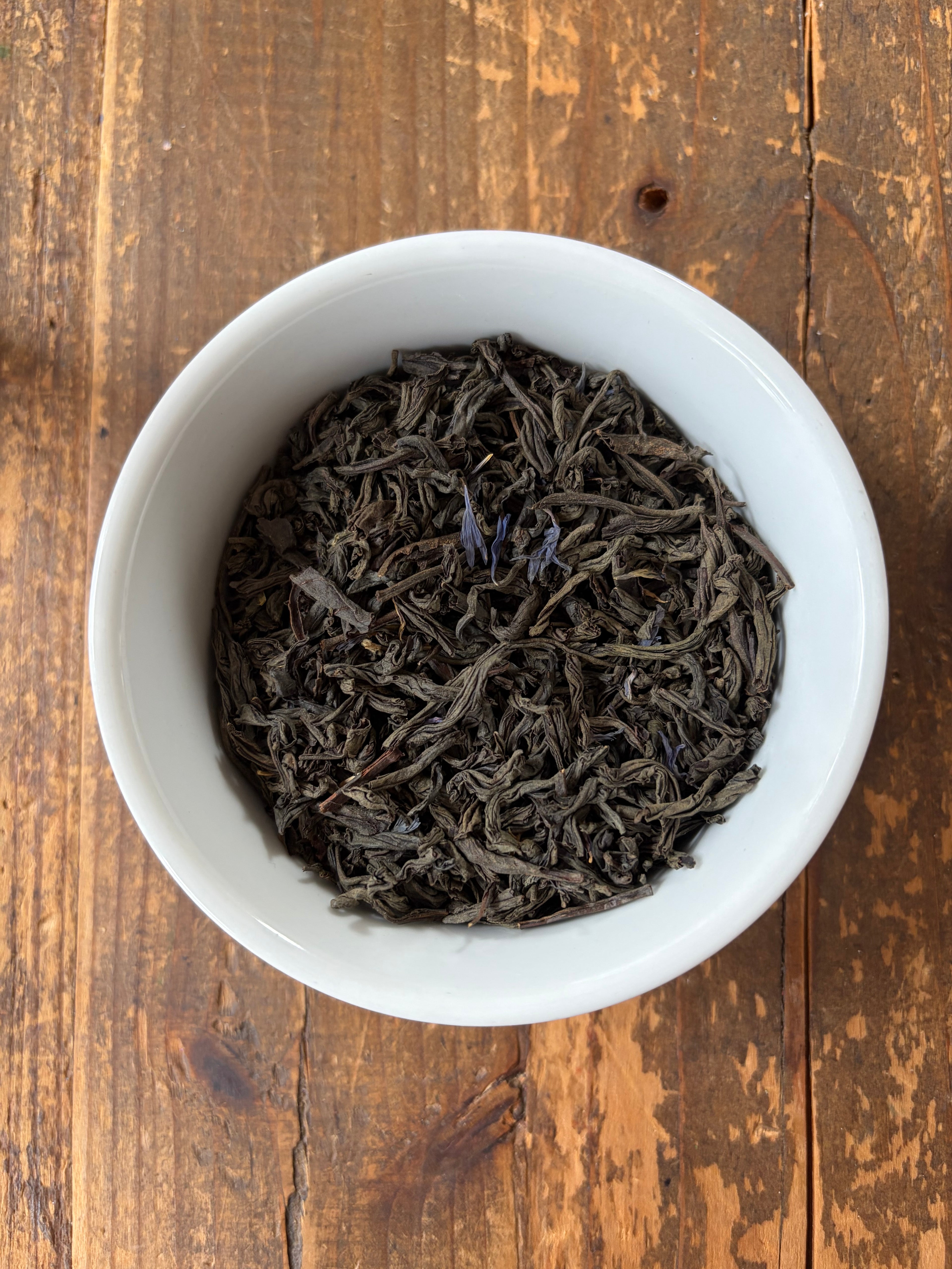 White bowl filled with Earl Gray tea leaves on a wooden surface