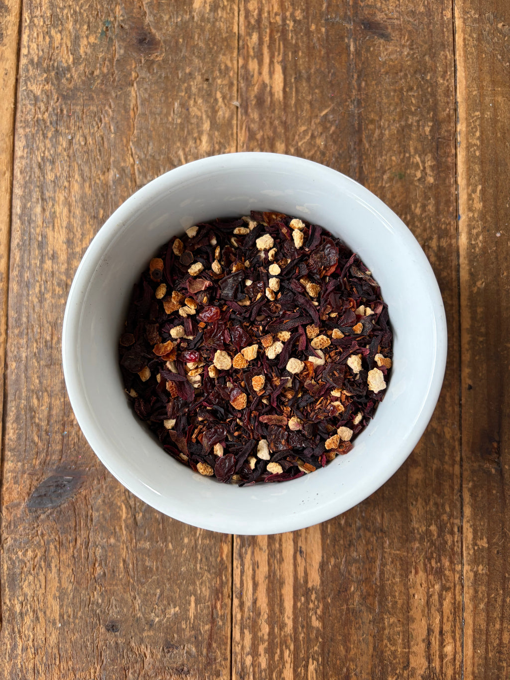 White bowl filled with hibiscus berry rooibos tea leaves on a wooden surface