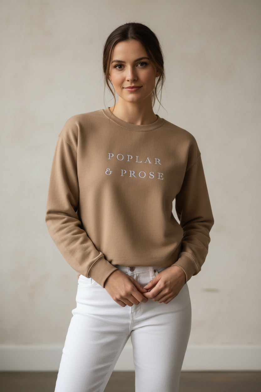 Latte sweatshirt with 'Poplar & Prose' text worn with white denim pants, neutral background