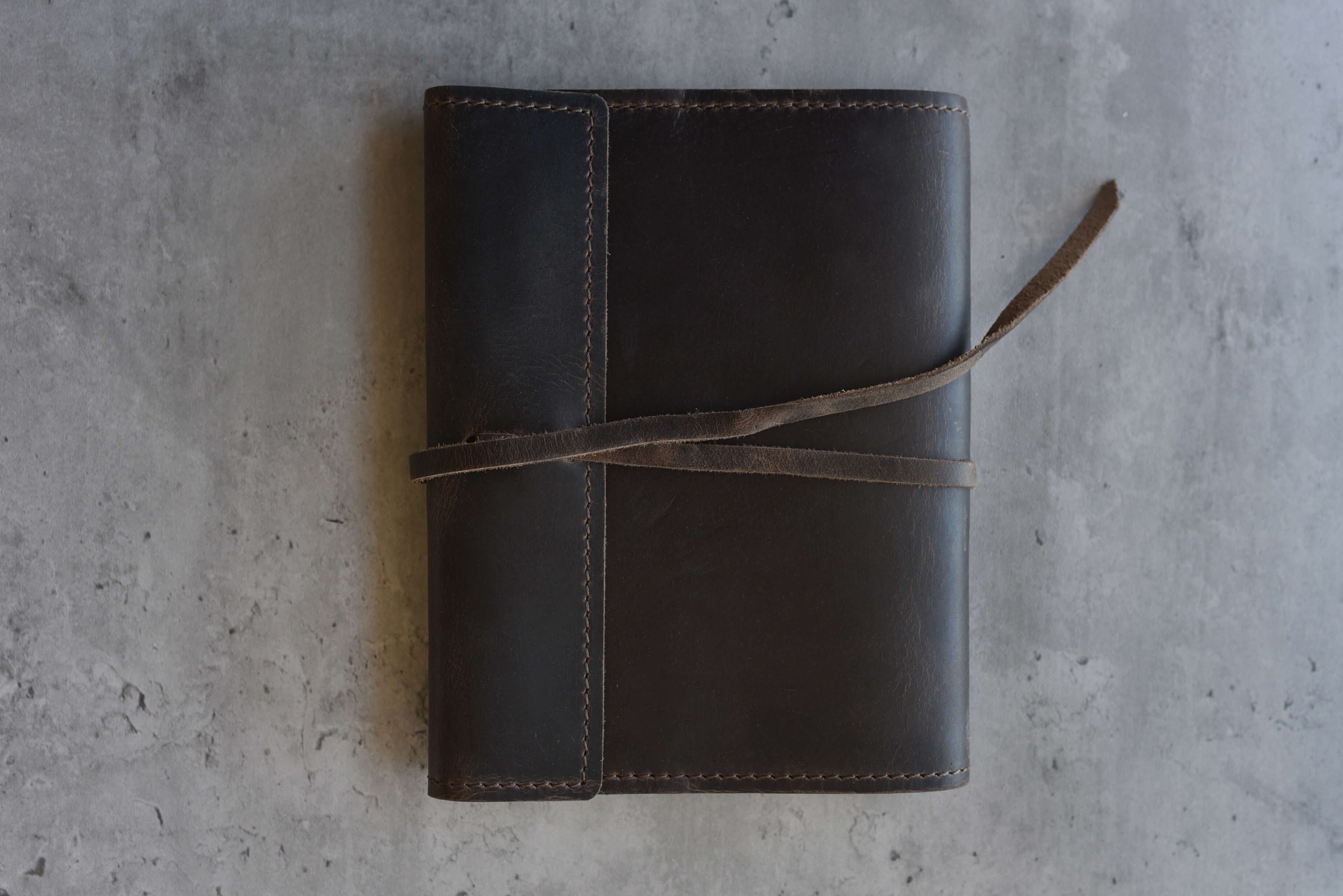 Brown leather notebook with a strap on a gray concrete surface