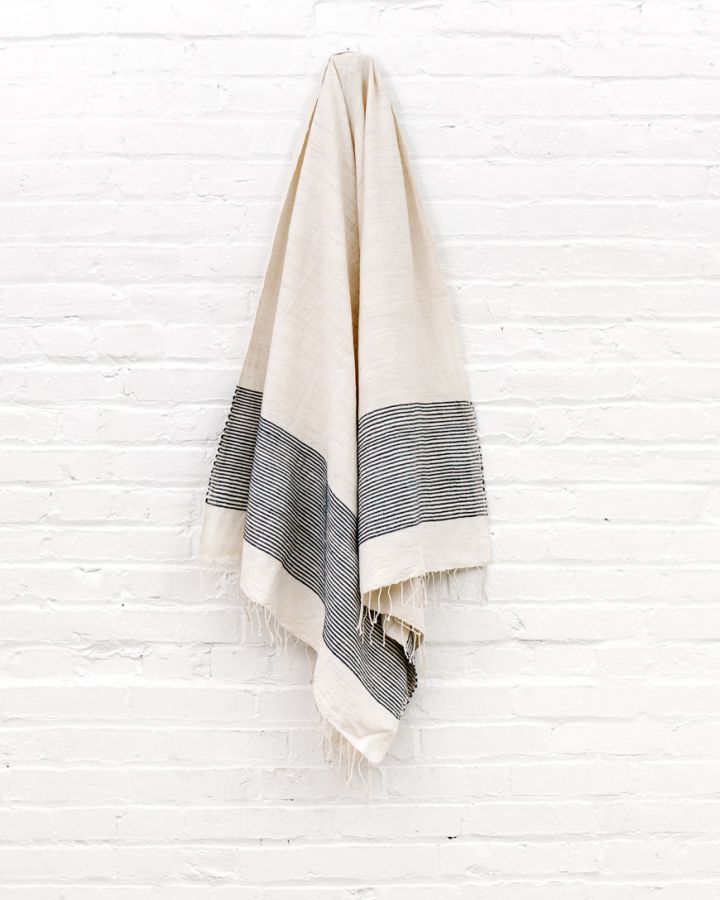 White-cream towel with navy stripes hanging on a white wooden wall