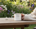 Person holding a mug with 'out past the pages' text in a garden setting
