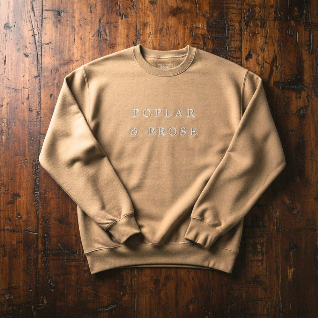 Beige sweatshirt with 'Poplar & Prose' text on a wooden surface
