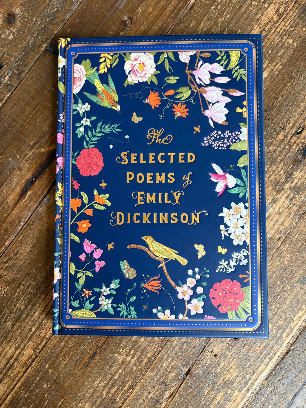 The Selected Poems of Emily Dickinson hardcover book with a navy blue floral cover, placed on a rustic wooden surface.