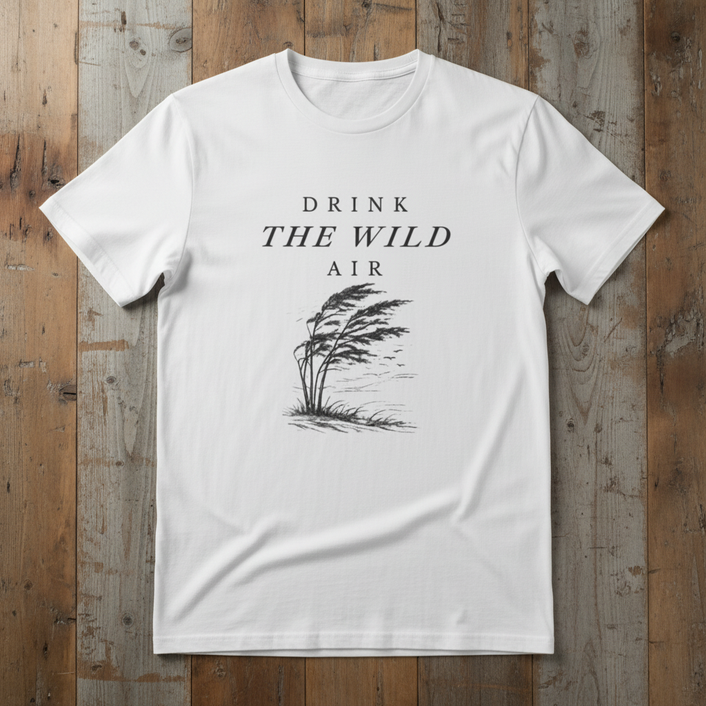 White t-shirt with 'Drink the Wild Air' text and tree graphic on wooden surface