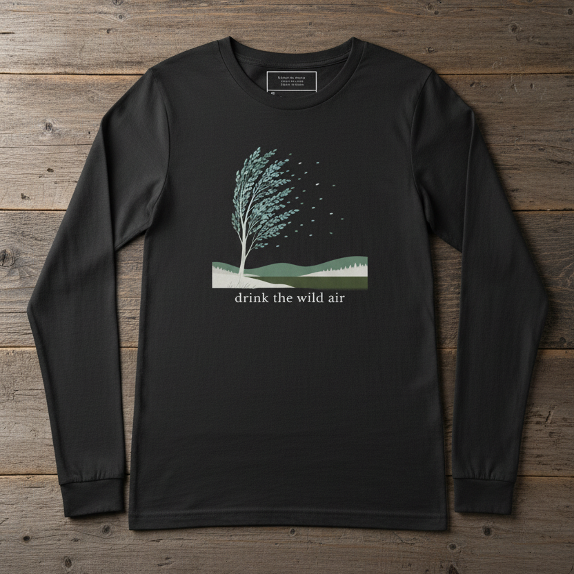 black long sleeve tee with tree blowing in the wind, hills illustration, and 'drink the wild air' on a reclaimed wood surface
