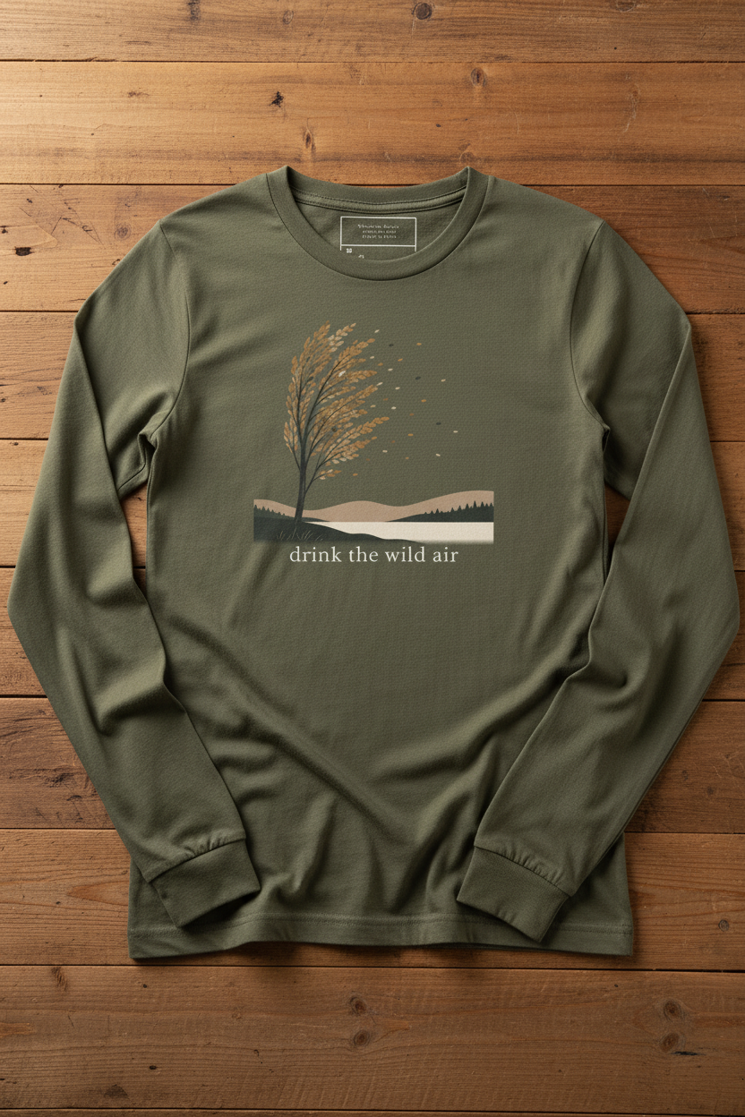 green long sleeve shirt with sweeping tree illustration, hills, and 'drink the wild air' on a reclaimed wood table
