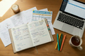 An open planner or journal with handwritten notes lies on a wooden desk alongside printed schedules, a laptop showing a calendar, colored highlighters, a candle, and a mug of tea. A sheet at the top reads 'SOCCER SEASON 2026'.