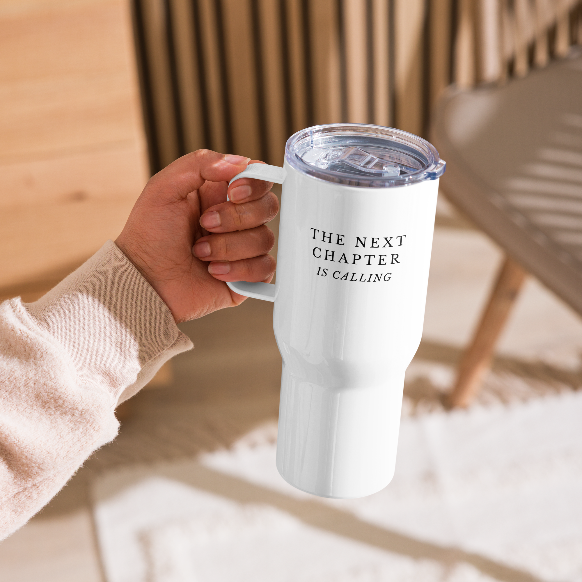Hand holding a white tumbler with 'The Next Chapter is Calling' text on a blurred background 25 oz